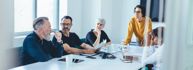 Eine Gruppe von Geschäftsleuten hat eine Teambesprechung in einem Sitzungssaal. Ein älterer Geschäftsmann bringt seine Ideen während einer Besprechung im Konferenzraum vor. - JLPSF13104