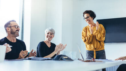 Geschäftsleute klatschen nach einer erfolgreichen Brainstorming-Sitzung im Sitzungssaal in die Hände. Eine Gruppe von Männern und Frauen applaudiert nach einer produktiven Sitzung. - JLPSF13109