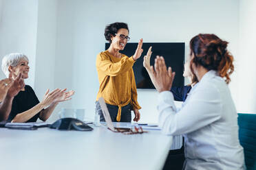 Happy business team in casual clothes at conference table giving high fives to each other, celebrating success. Business team starting a new project. - JLPSF13110