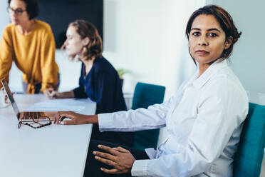 Confident young woman sitting at a business presentation with colleagues in boardroom. Female with coworkers in conference room looking at camera. - JLPSF13113