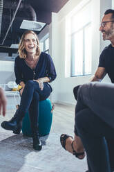 Woman smiling during a discussion in office. Business people sitting in a circle and sharing ideas in a modern office. - JLPSF13120