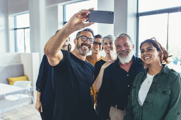 Erfolgreiches multirassisches Geschäftsteam, das zusammen ein Selfie macht. Reifer Geschäftsmann, der ein Selfie mit seinem Team in einem modernen Büro macht. - JLPSF13129