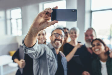 Geschäftsleute, die ein Selfie im Büro machen. Geschäftsteam, das gemeinsam ein Selfie bei einem Startup macht, mit Fokus auf das Mobiltelefon. - JLPSF13134