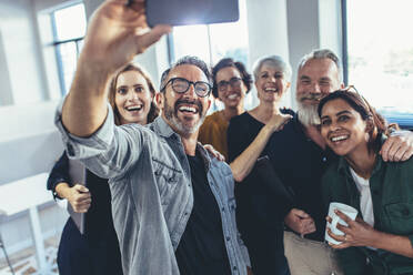 Business people taking selfie with phone and smiling. Successful business team taking selfie together in office. - JLPSF13135