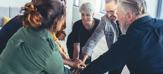 Team work and cooperation concept, people staking their hands on top of each other and smiling. Business people joining hands showing unity. - JLPSF13140