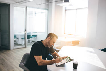 Mature businessman working on his digital tablet in a bright office. Entrepreneur checking emails on his tablet computer. - JLPSF13146