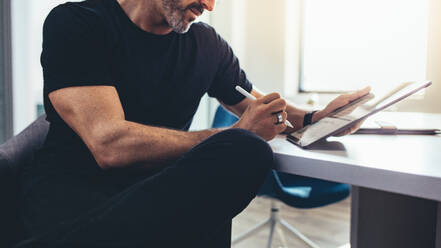 Mature businessman working on digital tablet in office. Mature man working in office with a tablet computer while sitting at table. - JLPSF13151