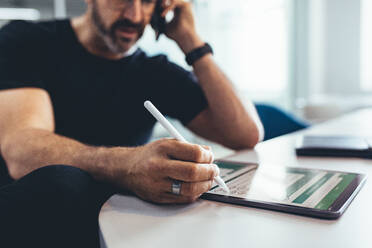 Businessman working on digital tablet and talking on phone. Male entrepreneur checking financial reports on his tablet computer and talking on phone. - JLPSF13155