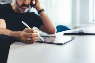 Reifer Mann, der am Handy spricht und an seinem digitalen Tablet arbeitet. Geschäftsmann, der im Büro arbeitet, konzentriert sich auf digitales Tablet und Stift. - JLPSF13156