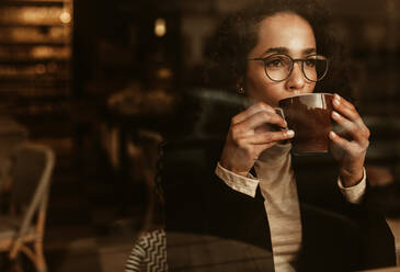 Woman wearing glasses drinking coffee and looking away. Female sitting inside cafe having a cup of coffee. - JLPSF13161