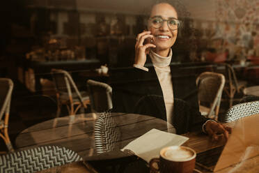 Woman sitting at cafe and talking on mobile phone. Businesswoman talking with client while working from a cafe. - JLPSF13167