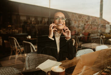 Frau, die ein Mobiltelefon in einem Café benutzt. Frau, die in einem Café sitzt und mit einem Laptop und einer Tasse Kaffee auf dem Tisch telefoniert. - JLPSF13168