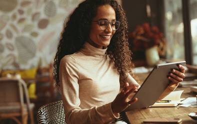 Frau sitzt im Café und benutzt ihr digitales Tablet. Lächelnde Frau in Freizeitkleidung arbeitet an ihrem Tablet-PC in einem Café. - JLPSF13174