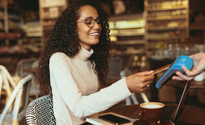 Lächelnde Frau, die ihre Rechnung in einem Café kontaktlos mit ihrer Kreditkarte bezahlt. Weibliche Kundin, die in einem Restaurant eine Kartenzahlung vornimmt. - JLPSF13182