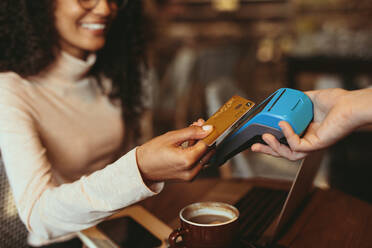 Frau beim kontaktlosen Bezahlen mit Karte in einem Café. Weibliche Kundin beim Bezahlen mit ihrer Kreditkarte in einem Café. - JLPSF13183