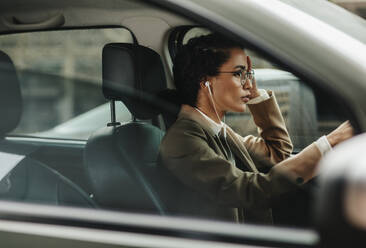 Businesswoman with earphones driving her car to office. Woman in formalwear driving to work. - JLPSF13186