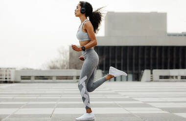 Totale Aufnahme einer Fitness-Frau beim Joggen in der Stadt. Frau in Sportkleidung und mit Kopfhörern beim Laufen im Freien. - JLPSF13213