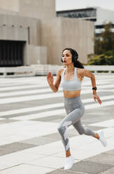 Sportswoman sprinting in the city. Woman in sportswear and headphones fast running outdoors. - JLPSF13216