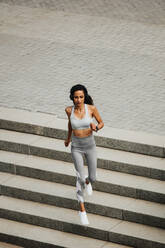 Hohe Winkelansicht einer sportlichen Frau, die im Freien die Treppe hinunterläuft. Frau in Sportkleidung läuft am Morgen. - JLPSF13220
