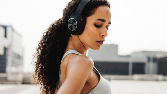 Sportliche Frau mit Kopfhörern im Freien stehend. Frau hört Musik mit Kopfhörern während einer Trainingspause. - JLPSF13222