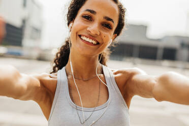 Glückliche Fitness-Frau, die ein Selfie im Freien am Morgen macht. Weibliche Athletin mit Kopfhörer, die in die Kamera schaut und lächelt. - JLPSF13228