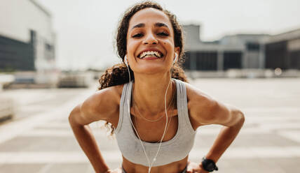 Fitness-Frau mit Kopfhörern, die in die Kamera schaut und lächelt. Fröhliche Läuferin in Sportkleidung. - JLPSF13229