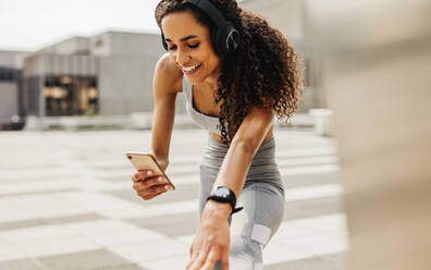 Fitness-Frau, die beim Training eine App auf ihrem Telefon benutzt. Lächelnde Frau beim Stretching-Workout und mit Smartphone. - JLPSF13233