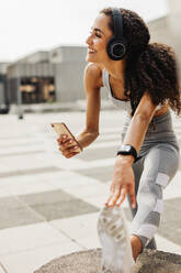 Frau beim Sport in der Stadt. Frau mit Kopfhörern hört Musik von ihrem Handy. - JLPSF13234