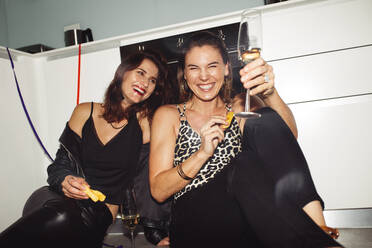 Glückliche Frauen, die sich zu Hause amüsieren und Wein genießen. Zwei fröhliche Frauen, die zu Hause auf dem Boden sitzen und eine Party feiern. - JLPSF13238