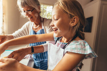 Granny and kid having fun cooking food in the kitchen. Happy girl learning to cook food with her grandmother wearing apron. - JLPSF13254