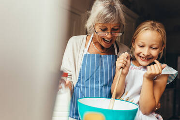 Happy grandmother and kid mixing a cake batter at home. Happy little girl stirring batter in a bowl with her granny standing by her side. - JLPSF13255