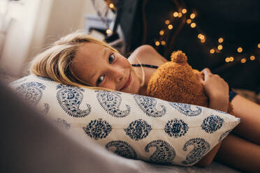 Lächelndes Kind auf dem Bett liegend, das sein Spielzeug hält. Nahaufnahme eines kleinen Mädchens zu Hause auf dem Bett liegend, das einen Teddybär hält. - JLPSF13262