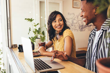 Two social media influencer meeting up at a cake and discussing over their new content. Man and woman sitting at cafe table with laptop. - JLPSF13265