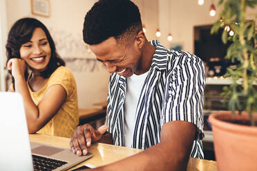 Young man smiling while talking with female friend at coffee shop. Two young creative people meeting at cafe. - JLPSF13266