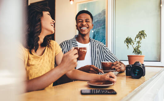 Freunde unterhalten sich und lächeln, während sie in einem Café Kaffee trinken. Mann und Frau trinken zusammen Kaffee mit einer Digitalkamera auf dem Tisch. - JLPSF13270