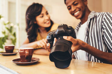 Junger Mann, der seiner Freundin im Café Bilder auf seiner Digitalkamera zeigt. Mann, der einer Frau im Café seinen neuen Inhalt auf einer Digitalkamera zeigt. - JLPSF13271