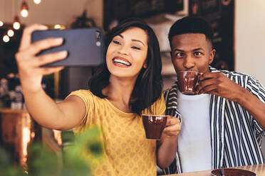 Frau nimmt Selfie mit Freund macht lustige Ausdrücke, während Kaffee trinken. Freunde nehmen Selfie mit Smartphone im Café. - JLPSF13275