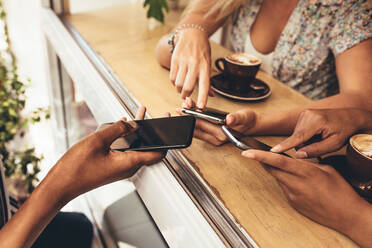 Ausschnitt von jungen Leuten, die ihre Geräte in einem Café miteinander verbinden. Nahaufnahme von Freunden, die das Wi-Fi nutzen, um ihre Mobiltelefone miteinander zu verbinden. - JLPSF13277