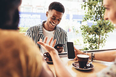 Eine Gruppe kreativer Menschen trifft sich in einem Café. Lächelnde junge Freunde sitzen im Café und benutzen Smartphones. - JLPSF13278