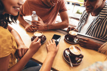 Eine Gruppe von kreativen Menschen trifft sich in einem Café und diskutiert über neue Inhalte für ihre sozialen Medien. Junge Männer und Frauen sitzen mit Kaffee und Handy am Kaffeetisch. - JLPSF13281