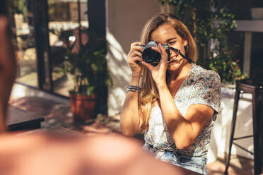 Eine Frau fotografiert ihre Freunde mit einer Digitalkamera, während sie in einem Café sitzt. Ein Mann lässt sich von einer Freundin für diese Social-Media-Posts fotografieren. - JLPSF13284