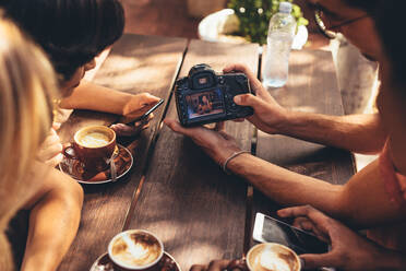 Ein Mann zeigt ein Bild auf seiner DSLR-Kamera seinen Freunden, die an einem Cafétisch sitzen. Eine Gruppe von Kreativen trifft sich in einem Café und sieht sich den Inhalt an. - JLPSF13285