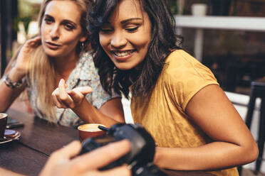 Frauen, die sich Fotos auf der Digitalkamera eines männlichen Freundes ansehen und sich unterhalten. Autoren von Social-Media-Inhalten treffen sich in einem Café. - JLPSF13287