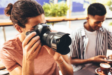 Man taking pictures for channel while sitting at cafe with friends. Friends meeting at cafe taking pictures. - JLPSF13288