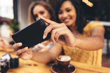 Nahaufnahme einer Frau, die ein Selfie mit ihrem Smartphone in einem Café macht. Fokus auf das Mobiltelefon. Ein Selfie - JLPSF13289