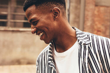 Nahaufnahme eines lächelnden afrikanischen Mannes in Freizeitkleidung. Ein junger Mann, der glücklich im Freien aussieht. - JLPSF13308