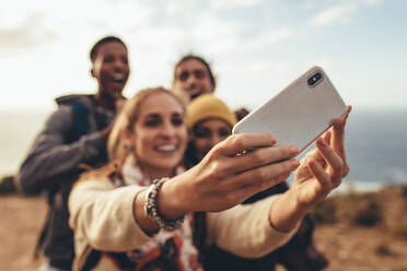 Frau nimmt Selfie mit Freunden auf Wanderschaft. Fokus auf weibliche Hände halten ein Smartphone und nehmen Selfie mit Freunden im Freien. - JLPSF13312