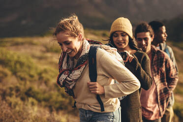 Eine Gruppe von Kreativen macht einen Wanderausflug, um Inhalte für soziale Medien zu erstellen. Junge Männer und Frauen wandern gemeinsam auf einem Bergpfad, während eine Frau ein Video mit ihrem Mobiltelefon aufnimmt. - JLPSF13318