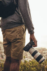 Mittlere Aufnahme eines Mannes, der mit seiner DSLR-Kamera mit Zoomobjektiv im Freien steht. Der Fotograf wandert in der Natur, um neue Inhalte für seine sozialen Medien zu finden. - JLPSF13324