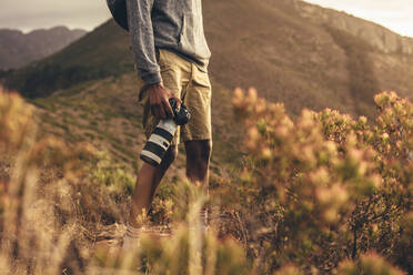 Mittlere Aufnahme eines Mannes, der mit seiner Spiegelreflexkamera auf einem Bergpfad steht. Der Fotograf wandert in der Natur, um neue Inhalte für seine sozialen Medien zu finden. - JLPSF13325